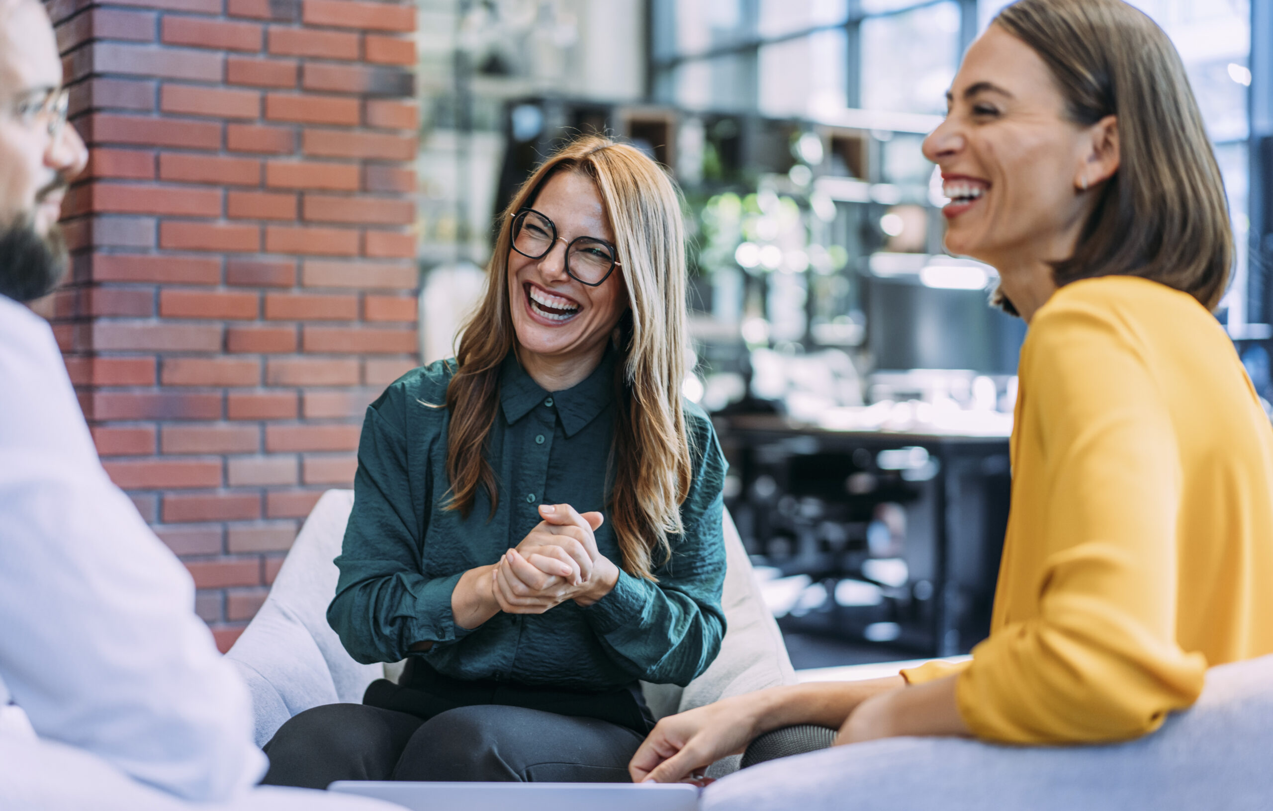 Drei Mitarbeitende unterhalten sich lachend in einem modernen Büro.