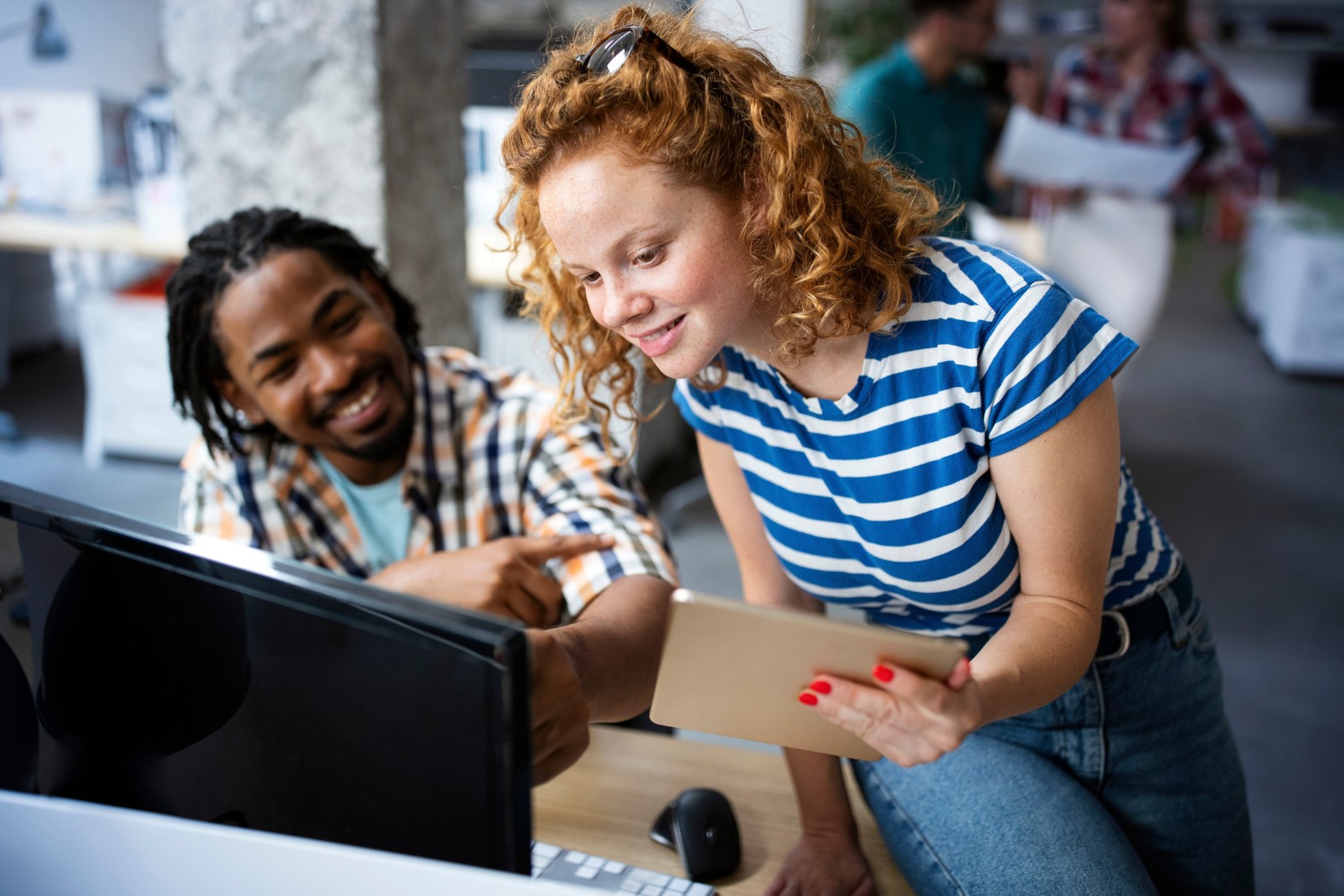 Zwei junge Mitarbeitende schauen gemeinsam auf einen Bildschirm im Büro.