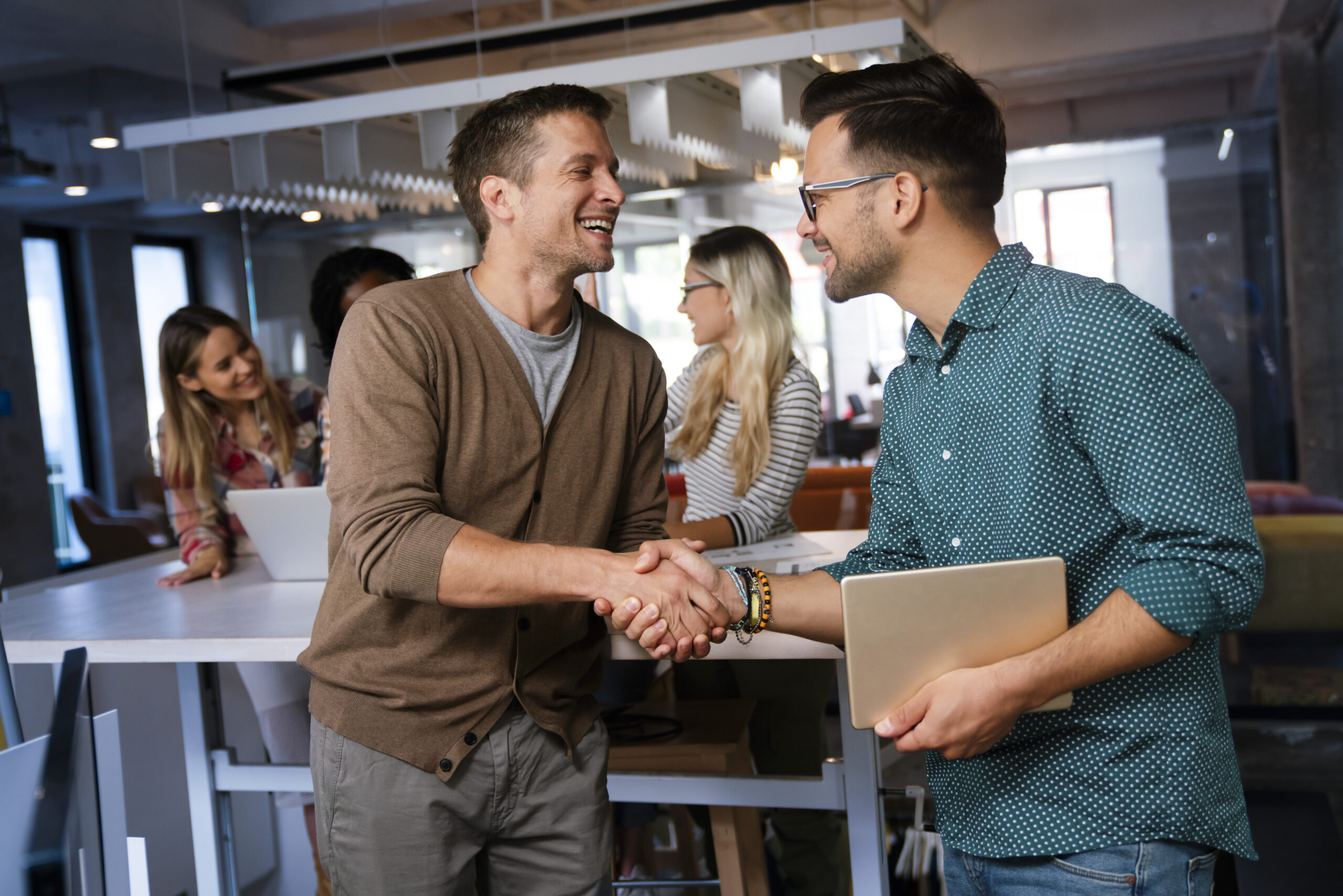 Zwei Kollegen geben sich lächelnd die Hand im Büro.