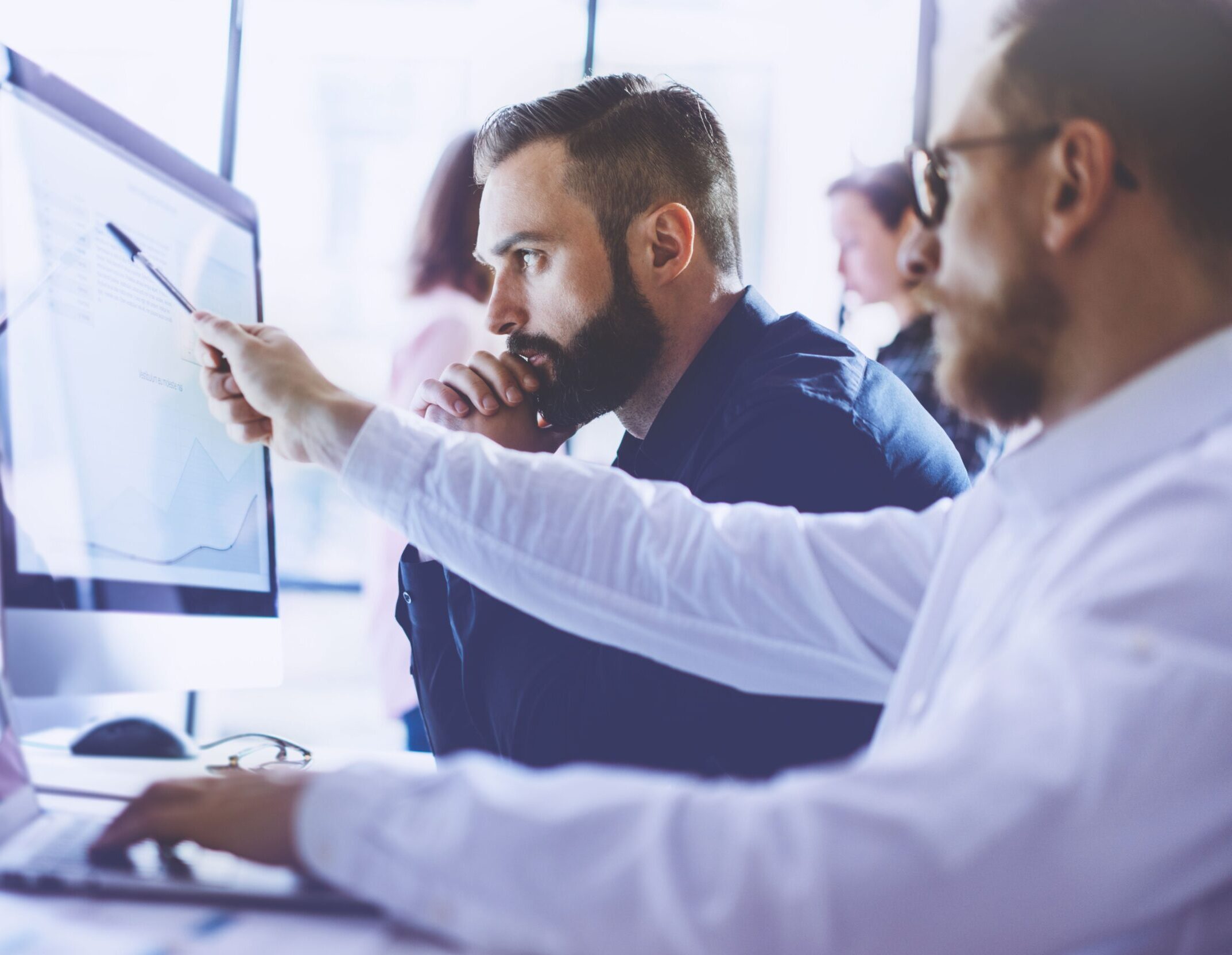 Zwei Männer im Büro analysieren Daten auf einem großen Monitor und besprechen gemeinsam die Ergebnisse.