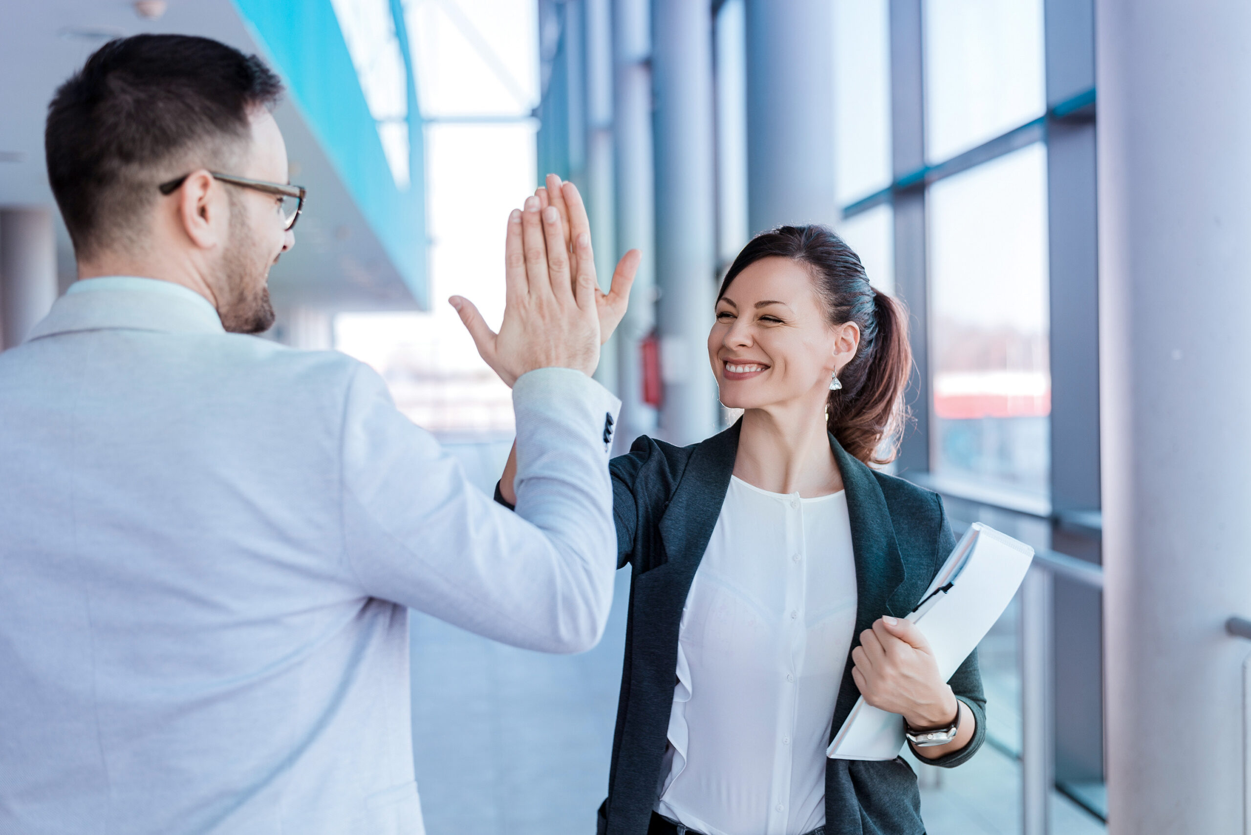 Ein Mann und eine Frau geben sich im Büroflur ein High Five.