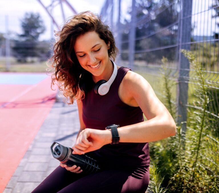 Eine junge Frau in Sportklamotten überprüft ihr Gesundheitswerte auf ihrer Smartwatch.